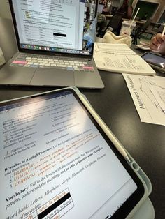 an open laptop computer sitting on top of a desk next to a tabletop filled with papers