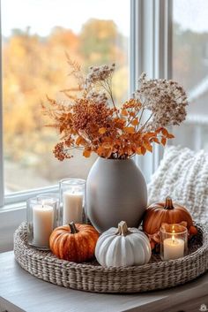 a basket with candles, flowers and pumpkins in it on a table next to a window