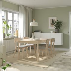 a dining room table and chairs in front of a large window with potted plants