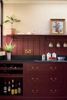 a kitchen with red cabinets and black counter tops, wine bottles on the shelves and a potted plant next to it