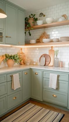 a kitchen with light green cabinets and white subway backsplash, potted plants on the counter