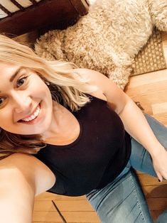 a woman sitting on the floor next to a teddy bear and looking up at the camera