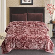 a bed covered in a red velvet comforter next to a night stand with flowers on it