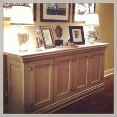 a white dresser with pictures on it in a living room next to two lamps and framed pictures