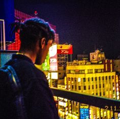 a man standing on top of a balcony next to a tall building with neon lights