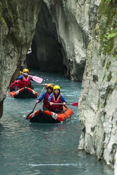 three people in rafts paddling through the water near large rock formations and cliffs