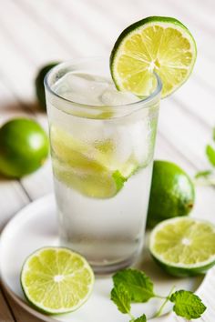 a glass filled with ice and limes on top of a white plate next to sliced limes