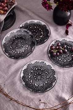 three black and white plates sitting on top of a table next to flowers in vases