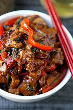 a white bowl filled with meat and veggies next to two red chopsticks