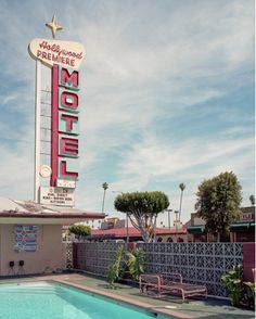 a motel sign next to a swimming pool and fenced in area with chairs around it