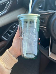 a person holding a starbucks cup in their hand while sitting in a car with the steering wheel behind them