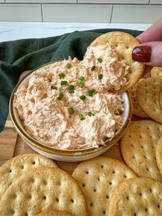 a cracker being dipped into a bowl of dip surrounded by crackers