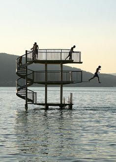 three people jumping off the top of a tower into the water