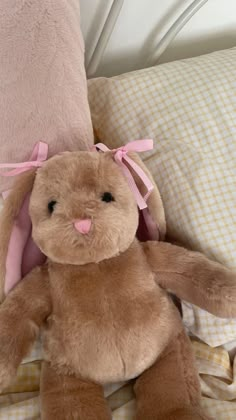 a brown stuffed rabbit sitting on top of a bed next to pillows and blankets with pink bows