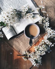 an open book and cup of coffee sit on a table with white flowers around it