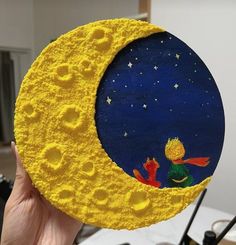 a hand holding up a painted moon with a little boy sitting on it's side