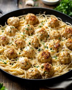 pasta with meatballs and parsley in a black skillet on a wooden table