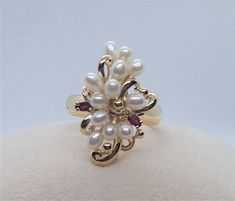 Unique 14kt yellow gold ring with 12 freshwater white pearls, 2 marquis-shaped rubies of approximately .06cttw. The pearls are in very good condition with clean lustrous nacre. The ring is 10.25 in size but it can be sized; the ring weighs 9.3 grams and is 4.8mm wide. This ring is in very good condition. The top of the ring is 27mm x 18mm. Please let us know if you have any questions. Rock N Gold Creations is located in San Diego, California, and has been serving customers locally, nationally, a Pearl Necklace Designs, Travel Jewelry Case, Travel Jewelry, Jewelry Inspo, Jewelry Case, Pearl Studs, Cluster Ring, Rock N, Yellow Gold Rings