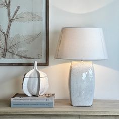 a white vase sitting on top of a wooden table next to a book and lamp