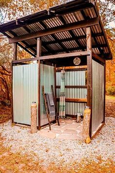 an outhouse in the middle of a wooded area with a bench and chair inside