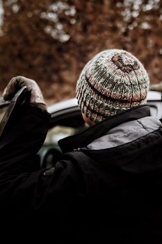 a person wearing a winter hat and jacket looking out the window of a car on a snowy day