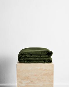 a folded green blanket sitting on top of a wooden block in front of a white wall