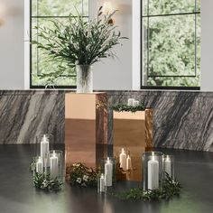 candles and flowers are arranged on a table in front of large windows with glass vases