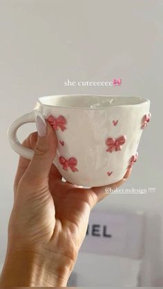 a hand holding a white cup with pink bows and hearts on the inside, in front of a white wall