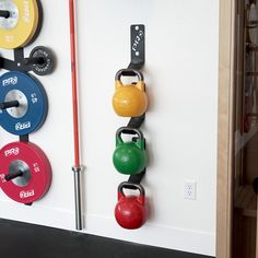 there are several different colored kettles hanging on the wall next to barbells