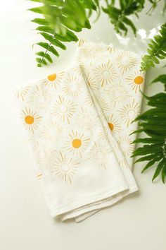 two napkins sitting next to each other on top of a white table with green leaves