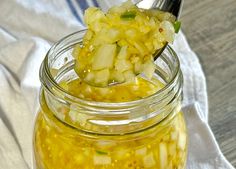 a spoon full of pickled up food on top of a white cloth next to a glass jar