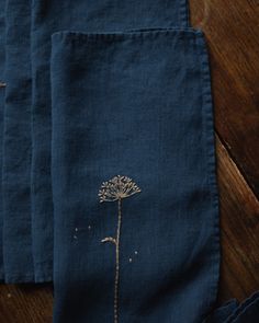 three blue linen napkins with a dandelion embroidered on them