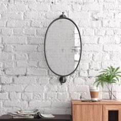 a white brick wall with a round mirror hanging on it's sideboard next to a wooden cabinet