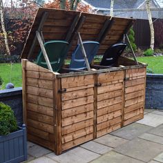 a large wooden storage box with two green trash cans in it's back yard