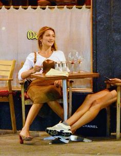 two women sitting at a table with wine glasses on the floor and one woman holding a cell phone