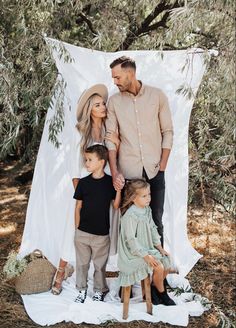 a man and two children are standing in front of a white sheet with an olive tree behind them