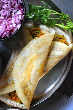 two burritos on a plate next to a bowl of chopped red onions and cilantro