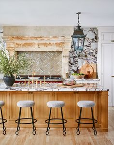 three stools sit at the center of a kitchen island in front of a fireplace