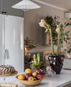 a kitchen counter topped with fruit and flowers next to a cake covered in icing