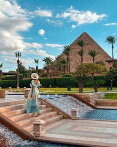 a woman in a hat is standing on some steps near a pool and pyramids