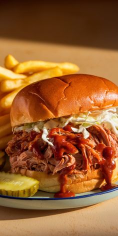 a pulled pork sandwich with coleslaw and pickles on a plate next to french fries