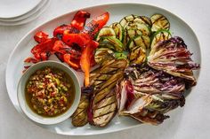 a white plate topped with grilled vegetables next to a bowl of dipping sauce on top of it