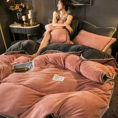 a woman sitting on top of a bed covered in pink and black sheets with pillows