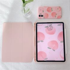 an ipad case with pink apples on it next to a flower vase and a cell phone