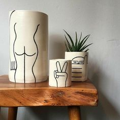 three ceramic pots with designs on them sitting on a wooden table next to a potted plant