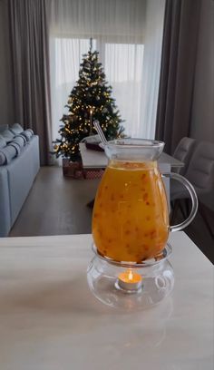 a glass pitcher filled with liquid sitting on top of a table next to a christmas tree