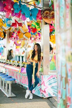 a woman standing in front of a carnival ride with lots of stuffed animals hanging from the ceiling