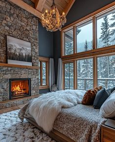 a bedroom with a stone fireplace in the corner and large windows on both sides that look out onto the snow covered mountains