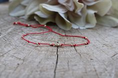 a red string bracelet sitting on top of a piece of wood next to a flower