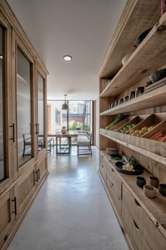 a long narrow hallway with wooden shelves and shoes on the floor, in front of a dining room table